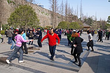 China, Jiangsu, Nanjing, Retired couples dancing beneath the Ming city wall at Xuanwu Lake Park Man in red sweater with arm extended to woman in pink sweater.