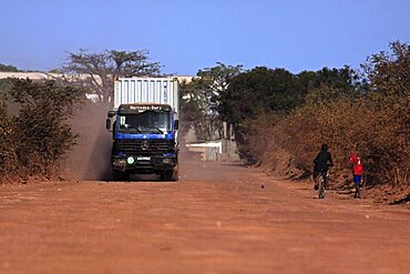 Gambia, Transport, Gambia heavy goods vehicle carrying sea container on unsurfaced red dirt road to terminal on the Bund Road.