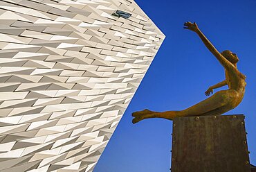 Ireland, North, Belfast, Titanic Quarter, Titanic Belfast Visitor Experience, 'Titanica' sculpture by Rowan Gillespie with a section of the building and blue sky in the background.