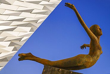 Ireland, North, Belfast, Titanic Quarter, Titanic Belfast Visitor Experience, 'Titanica' sculpture by Rowan Gillespie with a section of the building and blue sky in the background.,