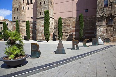 Spain, Catalonia, Barcelona, Scuplture by Joan Brossa in front of Barcelonas Roman wall, where the aqueduct once entered the city and spells out the word Barcino, the Roman name of Barcelona.