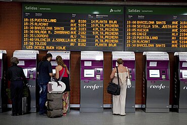 Spain, Madrid, Passengers using the self-service ticket machines in front of the departures board inside the terminus of the Atocha Railway Station