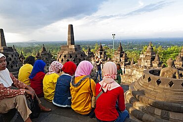 Indonesia, Java, Borobudur, A group of very colourfully dressed, seated Muslim women look out over the monument to the surrounding countryside.