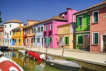 Italy, Veneto, Burano Island, Colourful row of house facades with boats on a small canal in the foreground.