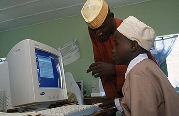 NIGERIA  Education Teacher leaning over boy sitting at a computer in a classroom African Kids Learning Lessons Nigerian Teaching Western Africa