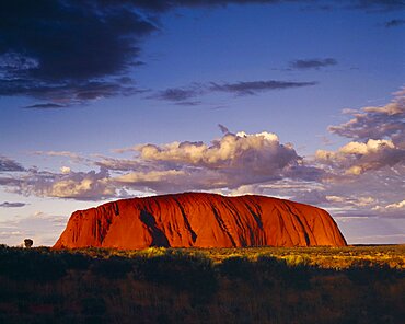 AUSTRALIA Northern Territory Uluru Ayers Rock.  Giant red rock formation at dusk overshadowed by storm clouds