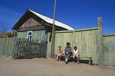 RUSSIA Lake Baikal Buryat woman and children outside painted wooden fence of house.  The Buryat are of Mongolian descent and are the largest ethnic minority group in Siberia.