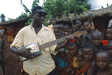 TANZANIA West Great Lakes Region Refugee children listening to boy playing guitar made from cooking oil can.