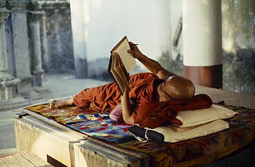 MYANMAR  Yangon Buddhist monk lying on raised platform and reading in Shwedagon Pagoda. Burma Rangoon Shwe Dagon