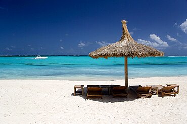 WEST INDIES St Vincent & The Grenadines Canouan Palapa thatched shelter and sunbeds on Godahl Beach at Raffles Resort with speedboat passing along the bay