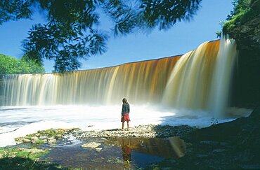 ESTONIA  Jagala Young woman standing in front of J?gala  steep horseshoe shaped waterfall between Tallinn and Lahemaa National Park