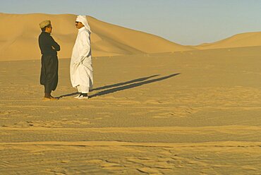 ALGERIA  Desert Two men standing in the desert in conversation casting strong shadows across the sand.