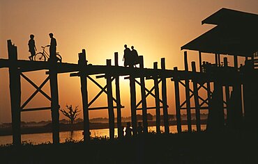 MYANMAR  Amarapura U Bein Bridge near Mandalay at sunset with silhouetted figures of monks  child and cyclist crossing. Burma Myanmar