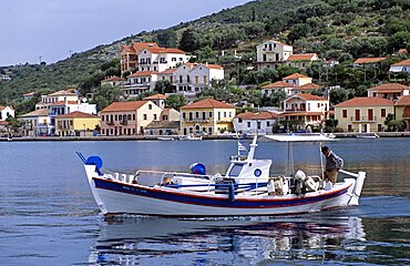 GREECE Ionian Islands Ithaca Vathi. Boat moving in harbour and Vathi town behind.  Travel Tourism Holiday Vacation Explore Recreation Leisure Sightseeing Tourist Attraction Tour Destination Vathi Ithaca Ithaka Ithica Ithika Ithaki Ithaci Greece Grecian Greek Ionian Sea Waterfront Waterside Water Calm Still Quiet Peaceful Picturesque Unspoiled Tranquility Tranquil Harbour Harbor Harbourside Harborside Hill Hillside Backdrop Vivid Vibrant Town Tradition Traditional Culture Cultural Community Buildings Houses Homes Residence Abode Dwellings Real Estate Property Apartments Fishing Boat Reflection Reflect Steep Man Gentleman Male Person Adult Fisherman Ethnic Business Work Working Worker Workplace Career Job Enterprise Enterprising Livelihood Occupation Moving Travelling Transport Transportation Foreground Interest Vacation Classic Classical Ellada Historical Male Men Guy Older Reflexion Southern Europe Traveling European History Male Man Guy