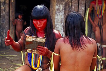 BRAZIL Mato Grosso Indigenous Park of the Xingu Young Panara women applying red karajuru face and body paint in preparation for dance.   Formally known as Kreen-Akrore  Krenhakarore  Krenakore  Krenakarore  Amazon American Brasil Brazilian Female Woman Girl Lady Indegent Kreen Akore Latin America Latino South America Female Women Girl Lady Immature