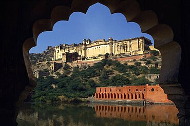 Amber Palace Fort near Jaipur situated on hillside above lake framed by scalloped edge of silhouetted window, Amber, Rajasthan, India