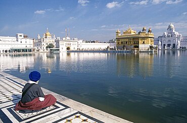 Sikh man sitting on marble walkway beside the sacred pool surrounding the Golden temple, Amritsar, Punjab, India