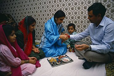 Woman tying thread on wrist of man during the Sacred Thread ceremony, The Hindu male rite of passage ceremony, England, United Kingdom