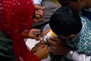 Woman tying thread on arm of boy during the Sacred Thread ceremony, The Hindu male rite of passage ceremony, England, United Kingdom