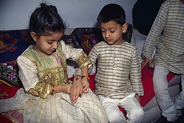 Young girl tying a thread to the wrist of a young boy during the Sacred Thread ceremony, The Hindu male rite of passage ceremony, England, United Kingdom