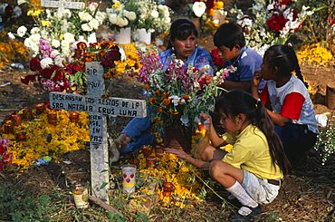 Tzurumutaro Cemetery, Children by family grave decorated with candles and flowers for the Day of the Dead, Patzcuaro, Michoacan, Mexico