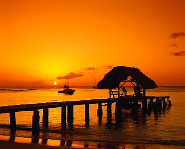 WEST INDIES Tobago Pigeon Point Wooden jet and boat silhouetted at sunset.