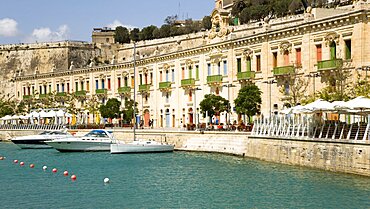 The waterfront redevelopment of old Baroque Pinto wharehouses below the bastion walls of Floriana beside the cruise ship terminal with boats moored alongside, Valletta, Malta