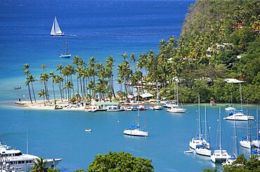 Marigot Bay The harbour with yachts at anchor and a yacht sailing out at sea beyond the small coconut palm tree lined beach of the Marigot Beach Club sitting at the entrance, Castries, St Lucia