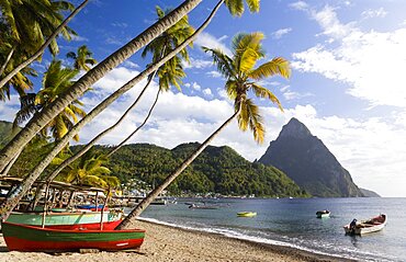 Fishing boats on the beach lined with coconut palm trees with the town and the volcanic plug mountain of Petit Piton beyond, Soufriere, St Lucia