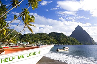 Fishing boats on the beach lined with coconut palm trees with the town and the volcanic plug mountain of Petit Piton beyond, A fishing boat in the foreground with the words Help Me Lord written on the bow, Soufriere, St Lucia