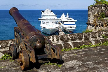 An old cannon pointing out to sea at Fort George with the Caribbean Princess and Aida Aura cruise ships moored below at the cruise ship terminal, St. Georges, Grenada, West Indies, Caribbean, Central America