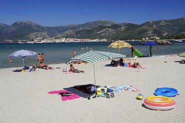 Bathers & sandy beach with St Florent old town in distance, France