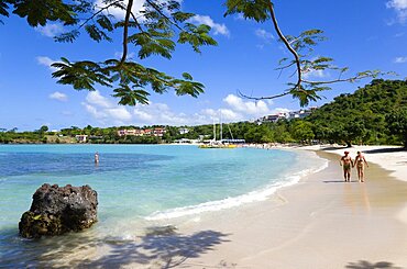 Gentle waves on BBC Beach in Morne Rouge Bay with tourists in the sea on the beach and aboard their tour catamaran in the aquamarine water, Caribbean