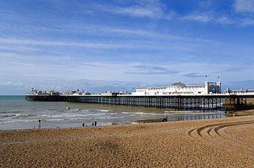 England, East Sussex, Brighton, The Pier at low tide with people on the shingle pebble beach.