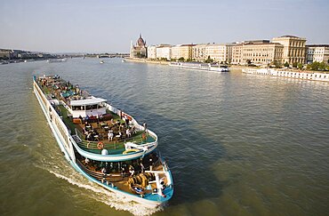 Hungary, Pest County, Budapest, pleasure cruise boat on the River Danube approaching Szechenyi Chain Bridge or Memory Bridge with Hungarian Parliament Building behind on right on Pest bank