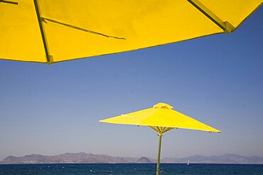 Greece, Dodecanese, Kos, bright yellow parasols on beach outside Kos Town with view towards distant coastline beyond