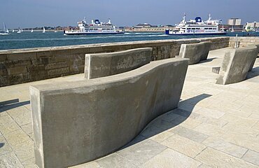 England, Hampshire, Portsmouth, Seats on the Millenium Walk with Isle Of Wight ferries and yachts passing through the harbour entrance with HMS Dolphin beyond.