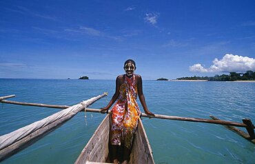 MADAGASCAR  Nosy Be Young girl on a pirogue canoe wearing a colourful sarong and with her face painted.  Turquoise sea.