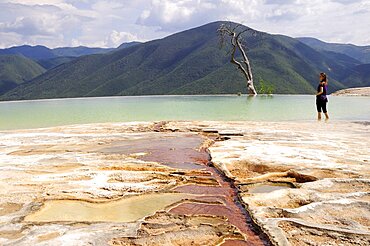 Female tourist standing in limestone pool with view towards mountainous landscape densely covered with trees,  Hierve el Agua, Oaxaca, Mexico