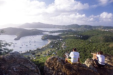 WEST INDIES Antigua General Couple sitting on rocks on hillside above Ordnance bay on the right and Tank Bay on the left.