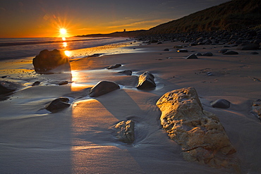 Golden early morning sunshine lights up the sandstone boulders on Dunstanburgh beach, Northumberland, England, United Kingdom, Europe