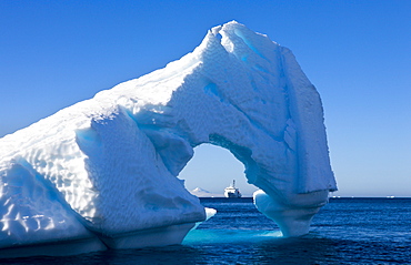 Looking through an Antarctic iceberg arch to the Akademik Ioffe research ship on the horizon, Antarctica, Polar Regions