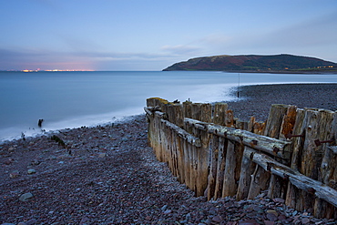 Weathered coastal defences at Porlock Weir in Exmoor National Park, with the evening lights of Wales visible across the Bristol Channel, Somerset, England, United Kingdom, Europe