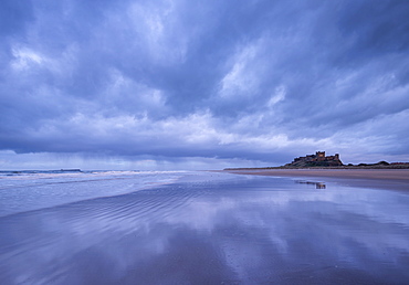 Storm clouds reflect on the deserted beach beside Bamburgh Castle in winter, Northumberland, England, United Kingdom, Europe