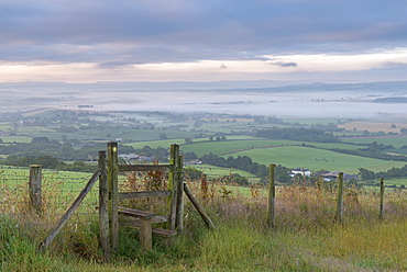 Footpath and stile through farmland with mist covered countryside beyond, Devon, England, United Kingdom, Europe