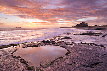 Heart shaped rockpool reflecting the colours of a beautiful pink sunrise, Bamburgh Castle, Northumberland, England, United Kingdom, Europe