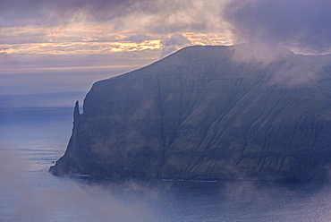 Sunset behind the Trollkonufingur (Troll Finger) and the immense sea cliffs of the island of Vagar, Faroe Islands, Denmark, Europe