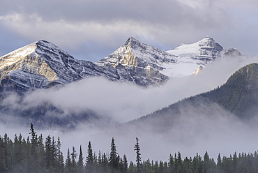 Early morning mist hangs in the wooded valleys below the snow capped mountains of the Canadian Rockies, Banff, Alberta, Canada, North America