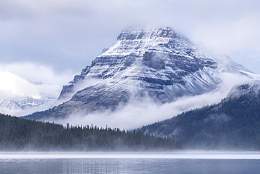 Snow dusted Bow Peak mountain surrounded by mist, viewed from across Bow Lake, Icefields Parkway, Alberta, Canada, North America