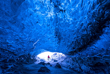 Man standing at entrance to an ice cave beneath a glacier, Iceland, Polar Regions